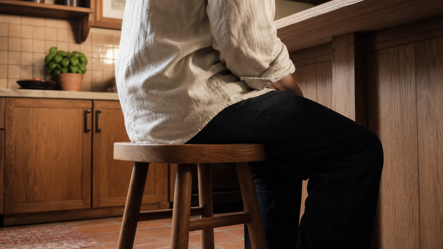 A candid photo of a person sitting on a bar stool, sliding their hands under their thighs to hide them.