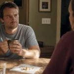 An unposed photo of a man sitting at a kitchen table looking slightly guarded during a quiet, intimate conversation.