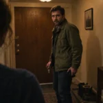 A man holding keys looks startled as he enters an apartment hallway, facing a woman seen from behind.