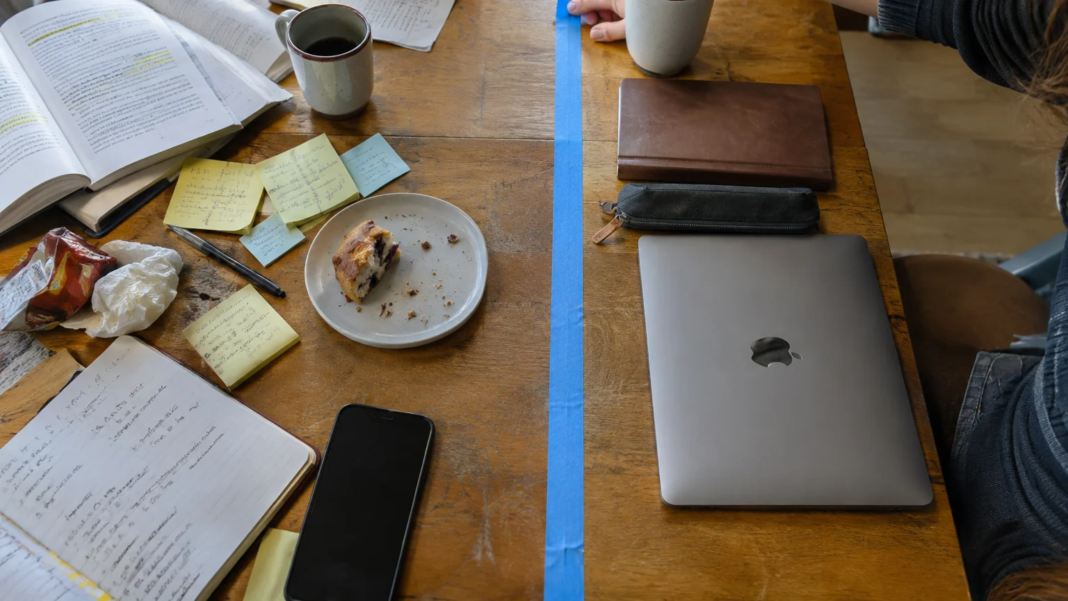 Blue painter's tape dividing a wooden table between scattered study notes and a neat laptop setup.